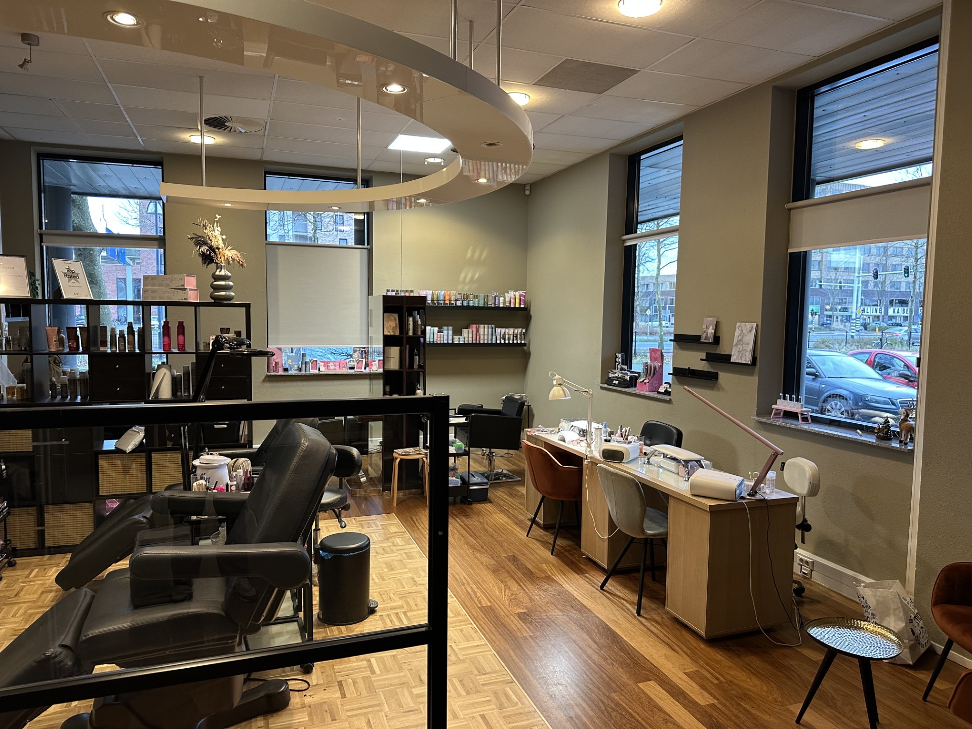 De salon: nageltafels bij de grote ramen, houten vloer en salie wanden