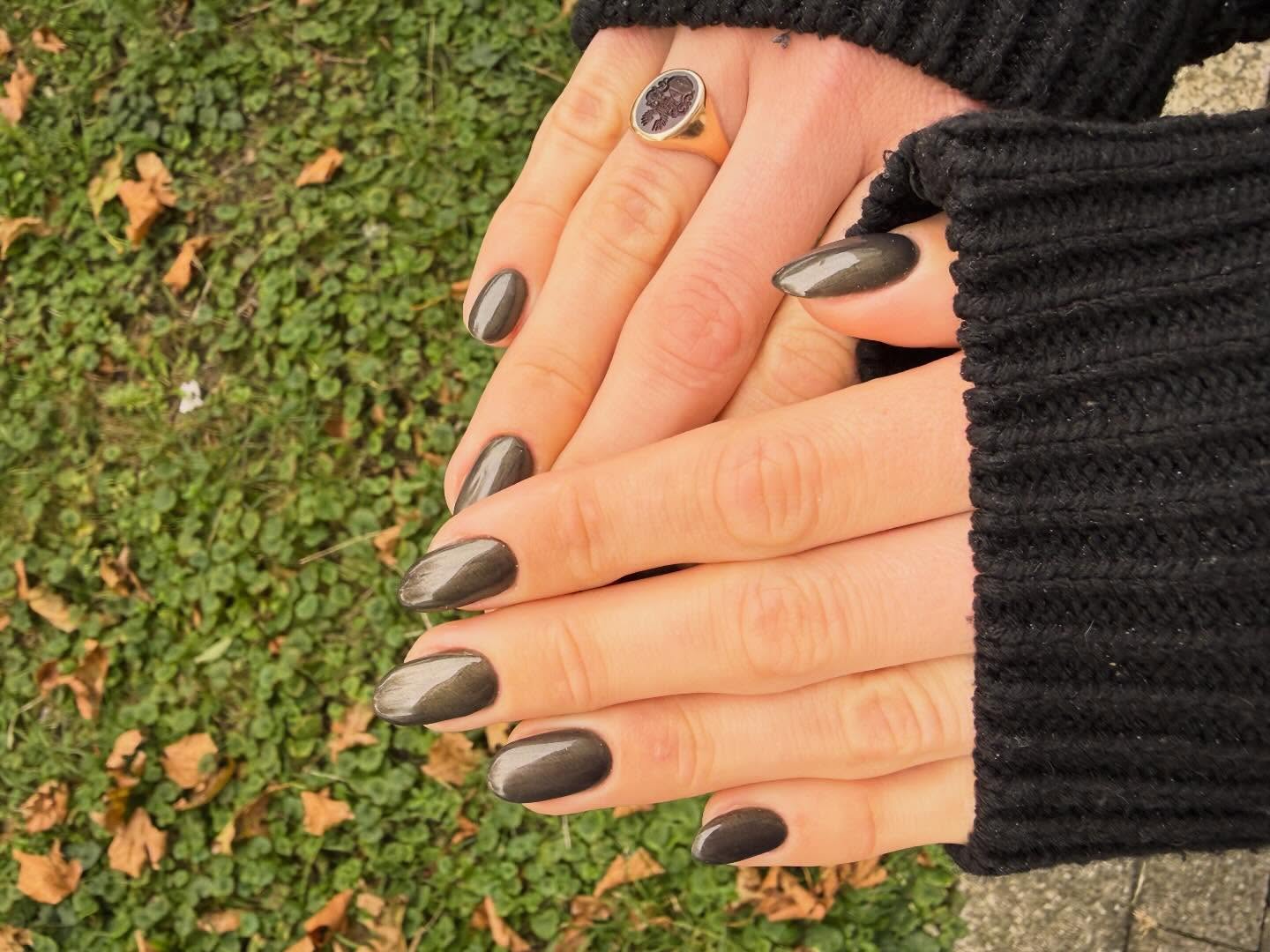 Antraciet cat-eye op amandelnagels, hand in een zwarte gebreide mouw